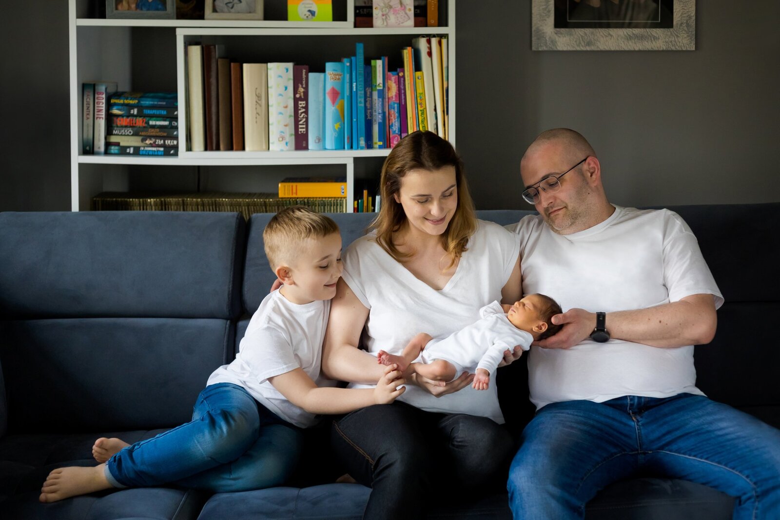 Lifestylowa sesja noworodkowa w domu - rodzina ubrana w jeansy i białe koszulki, a w roli głównej nowonarodzona dziewczynka