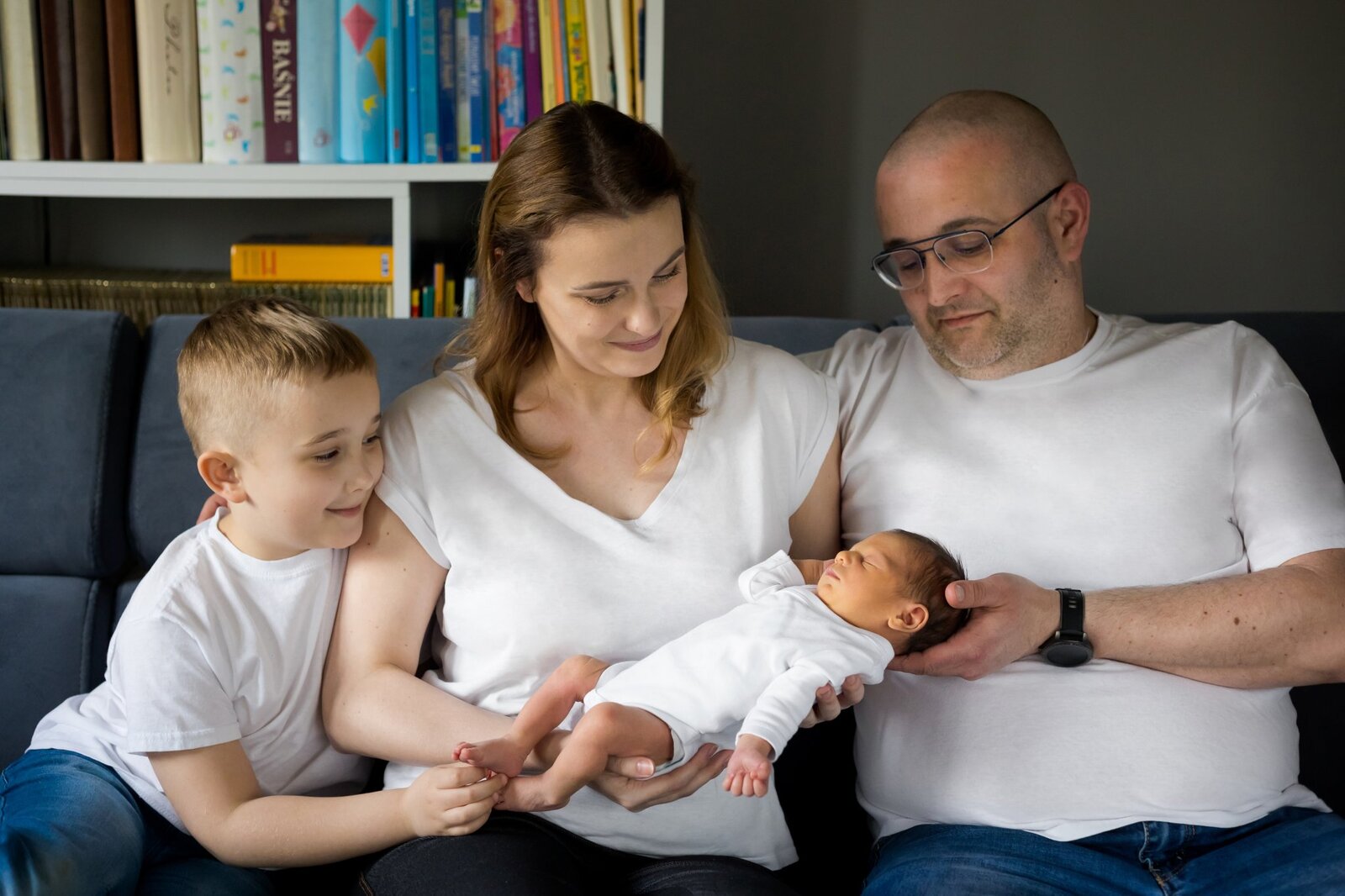 Lifestylowa sesja noworodkowa w domu - rodzina ubrana w jeansy i białe koszulki, a w roli głównej nowonarodzona dziewczynka